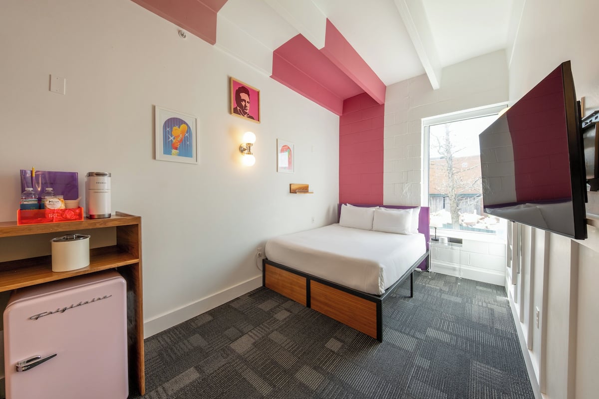 A hotel room with a bed, a small refrigerator, a TV, and a window with a view.