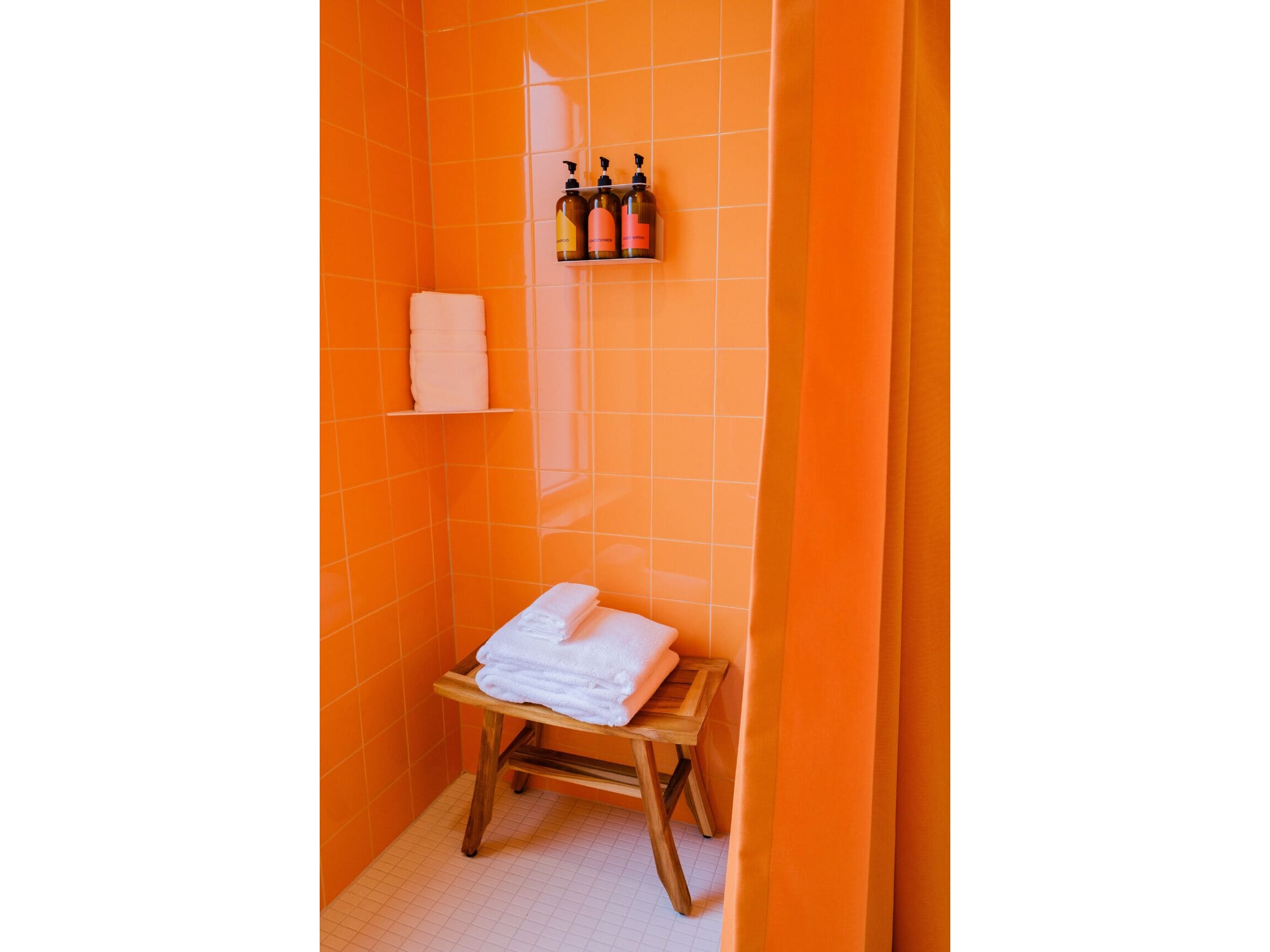 Um banheiro com azulejos laranja, um banco de madeira com toalhas e produtos de higiene pessoal em uma prateleira.