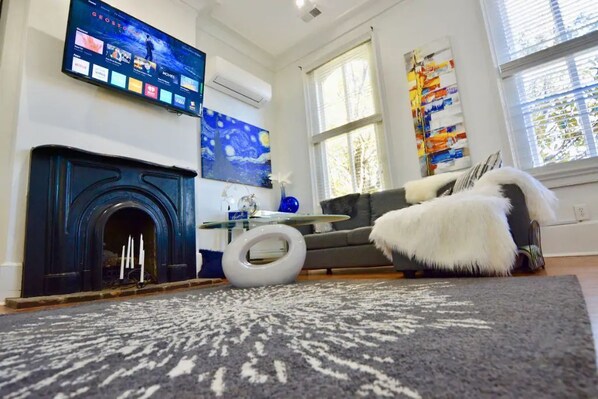 Een woonkamer met een open haard, een flatscreen televisie aan de muur, een bank en een vloerkleed.