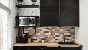 Une cuisine avec un mur de fond en briques, un four à micro-ondes, une machine à café et des armoires noires.