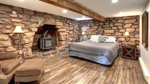 A bedroom with a stone wall, a fireplace, a bed, and a wooden floor. - Trail Mountain Cabin – Stunning Views, Hot Tub & Game Room (Lead)