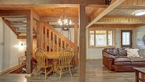 A wooden interior with a dining area, a staircase, and a living room with a leather sofa. - Trail Mountain Cabin – Stunning Views, Hot Tub & Game Room (Lead)