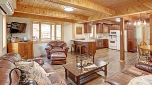 A spacious living area with a leather sofa, a coffee table, and a television mounted on the wall. - Trail Mountain Cabin – Stunning Views, Hot Tub & Game Room (Lead)