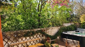 An outdoor seating area with wooden benches and cushions, a hot tub, and potted plants. - Meltime Share Mélanie's living space (Nîmes)