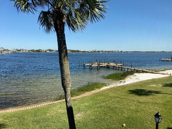 Vista al agua con un muelle que se adentra en aguas tranquilas, un área verde con un farol y un cielo despejado.