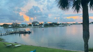 A waterfront view with a dock, boats, and lounge chairs on a grassy area. - Treasure on Pensacola Beach, views of Gulf, on Little Sabine Bay with boat docks (Pensacola Beach)