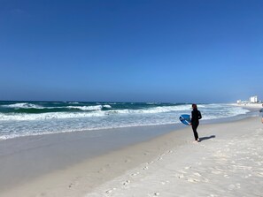 A beach with a person holding a surfboard, walking along the shore. - Treasure on Pensacola Beach, views of Gulf, on Little Sabine Bay with boat docks (Pensacola Beach)