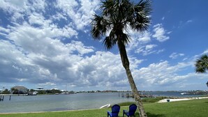 A grassy area with two blue chairs and a palm tree. - Treasure on Pensacola Beach, views of Gulf, on Little Sabine Bay with boat docks (Pensacola Beach)