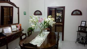A dining area with a wooden table, chairs, a vase with flowers, a mirror, and a framed certificate on the table.