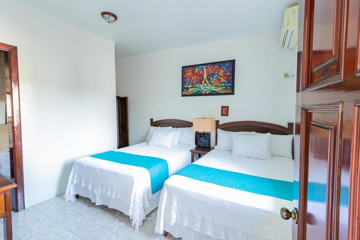Una habitación de hotel con dos camas, ropa de cama blanca y un cuadro colorido en la pared.