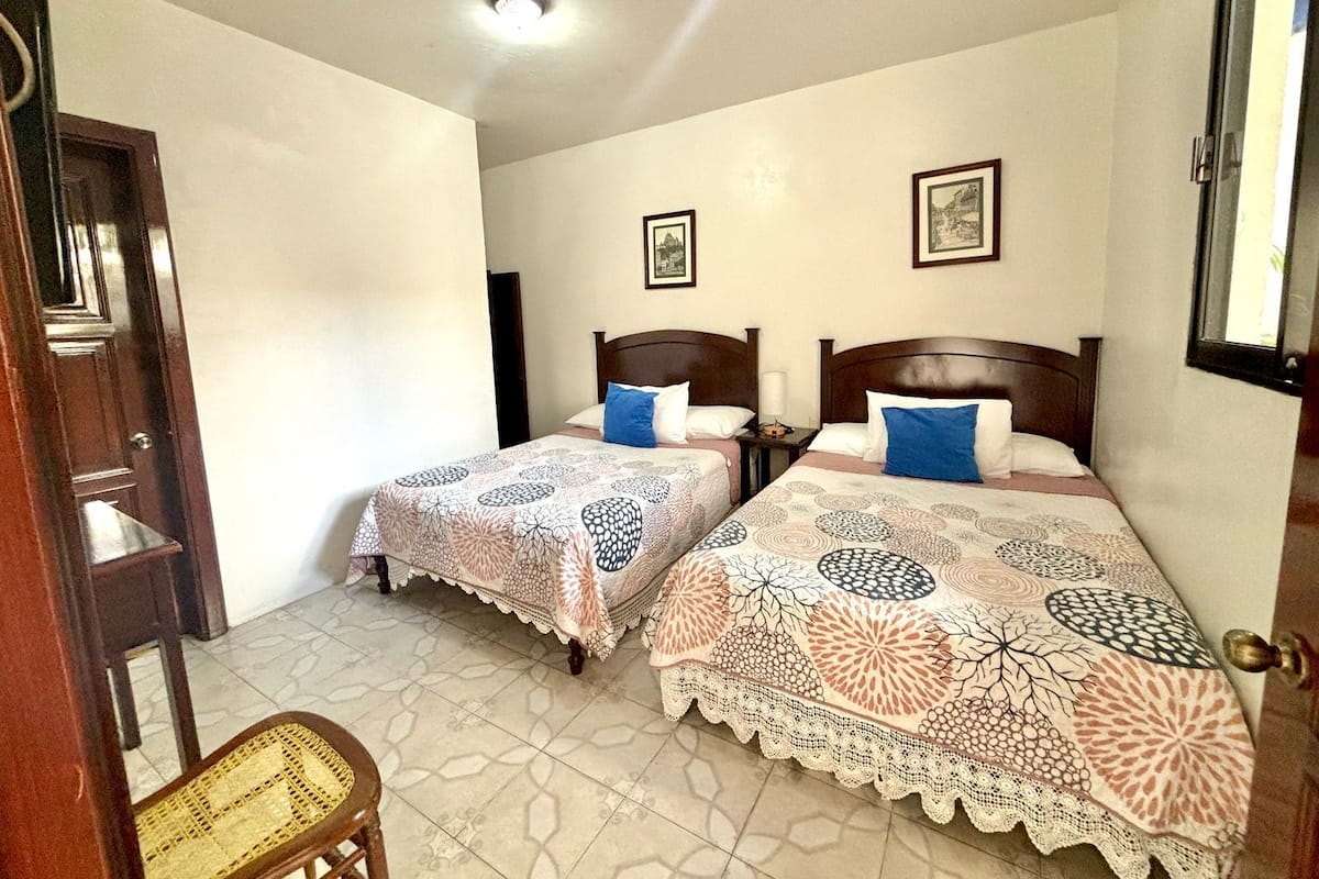 A room with two beds, a wooden door, a chair, and a ceiling light.