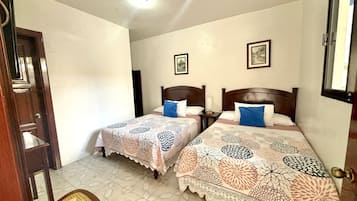 Una habitación con dos camas, una puerta de madera, una silla y una lámpara en el techo.