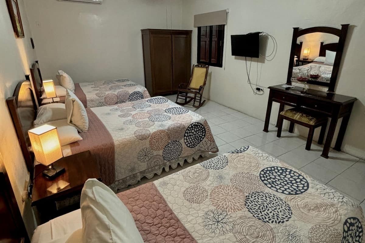 A hotel room with two beds, a ceiling fan, a TV, a desk, and a chair.