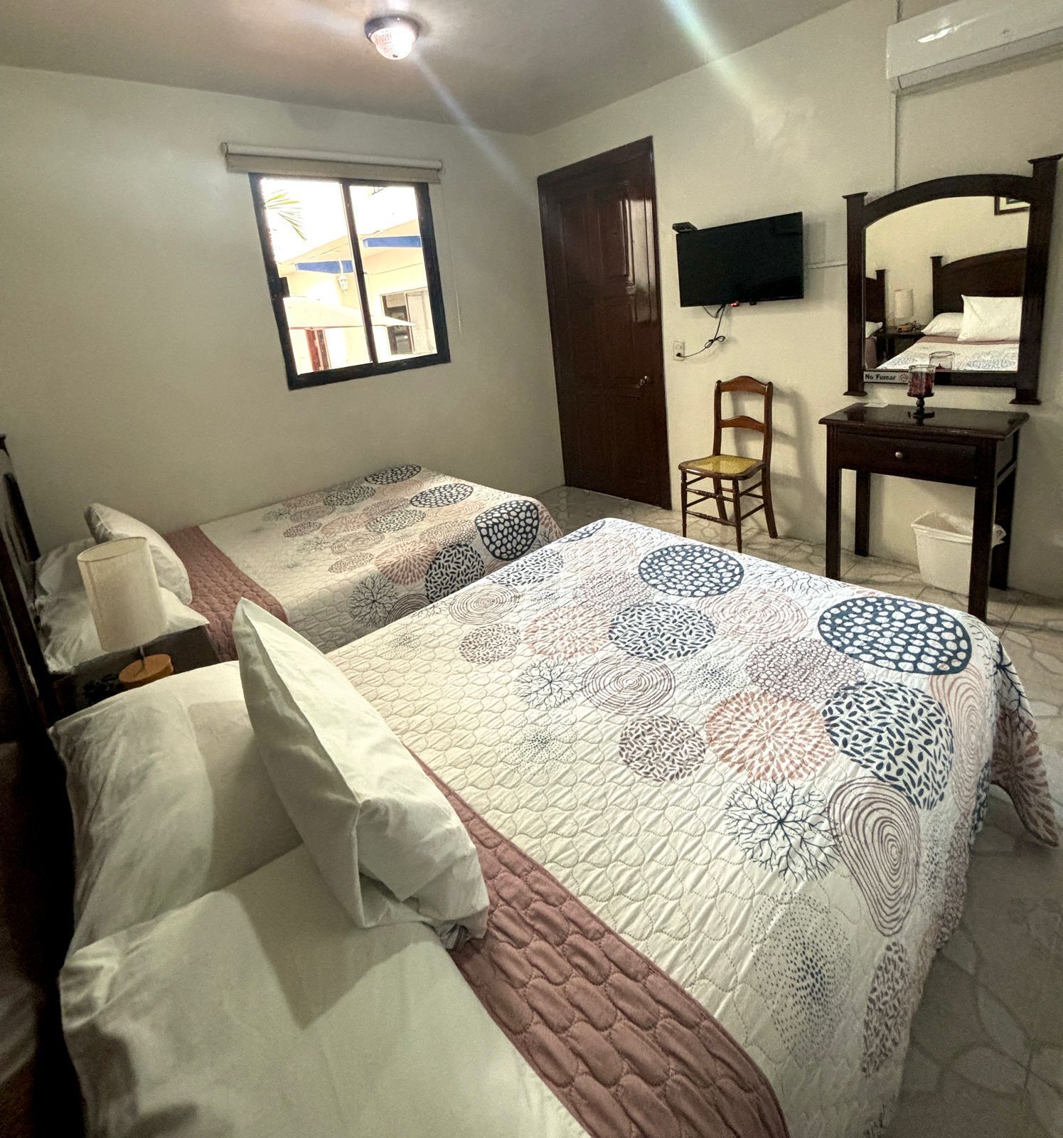 Une chambre avec deux lits, une fenêtre, une télévision, un bureau et une chaise.