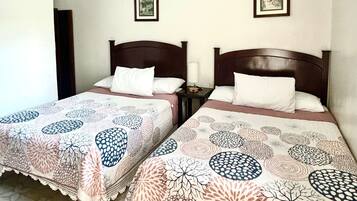 Dos camas individuales con cabeceros de madera, un edredón estampado y una mesita de noche con lámpara.
