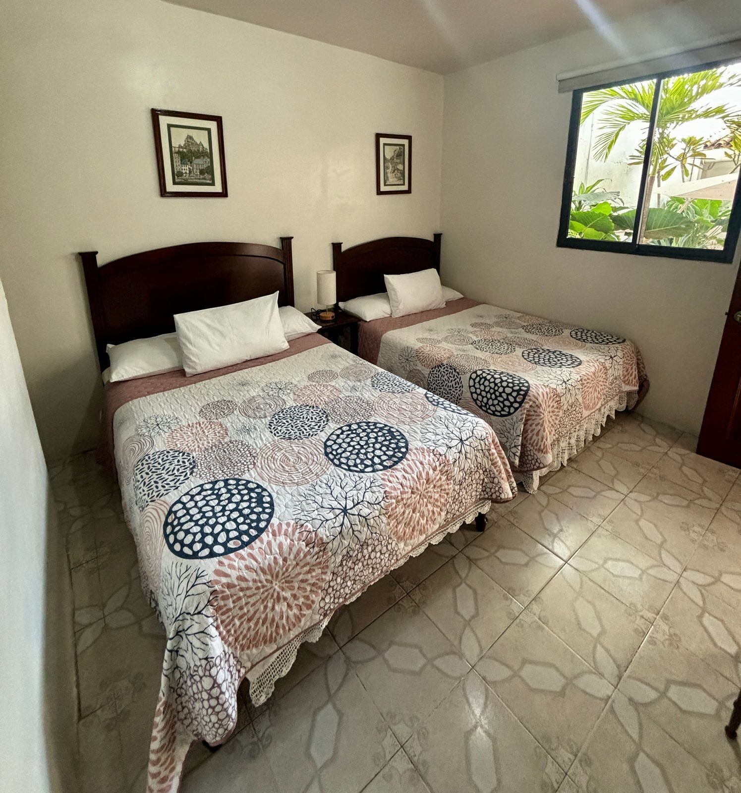A room with two beds, each with a patterned bedspread, a nightstand, and a framed picture on the wall.