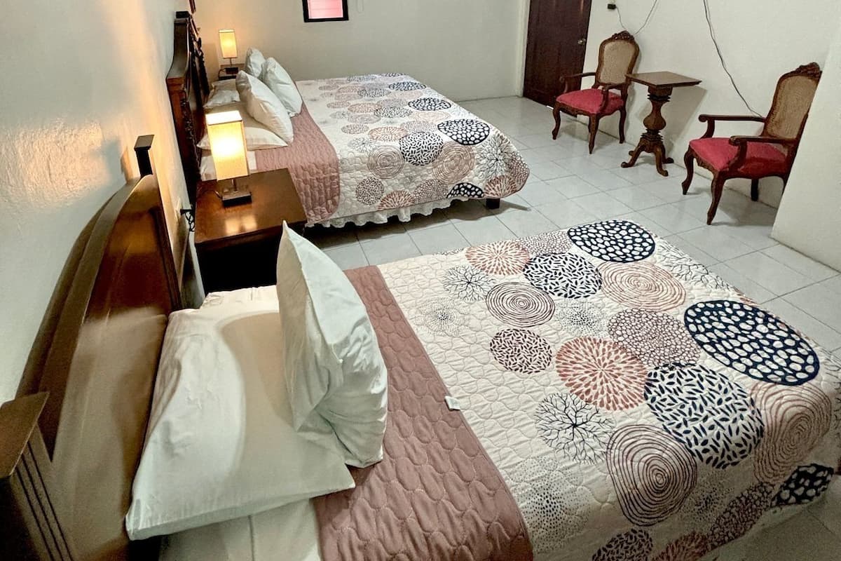 A hotel room with two beds, a ceiling fan, a TV mounted on the wall, and a small table with chairs.
