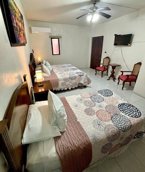 A hotel room with two beds, a ceiling fan, a TV mounted on the wall, and a small table with chairs.