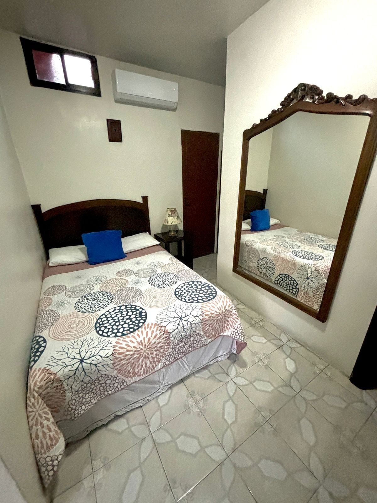 A bedroom with a bed, a nightstand, a mirror, and a window.