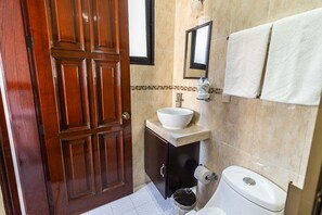 A bathroom with a wooden door, a sink with a mirror, a toilet, and two towels hanging on the wall.