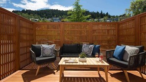 Eine Terrasse im Freien mit Holzzaun, einer schwarzen Couch, zwei Sesseln, einem Holztisch und einem Blumentopf.