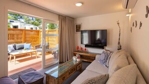 Ein Wohnzimmer mit einer Couch, einem Couchtisch, einem Fernseher und einer Glastür, die zu einem Außenbereich mit Holzzaun führt.