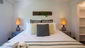 Ein ordentlich gemachtes Bett mit gestreifter Bettwäsche, zwei Nachttischlampen und einer an der Wand befestigten Pflanze.