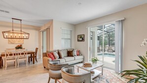 A spacious living room with a dining area, a large window with a view of a pool, and a ceiling fan.