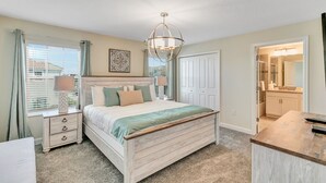 A bedroom with a bed, bedside tables, a chandelier, a wardrobe, and a bathroom visible through an open door.