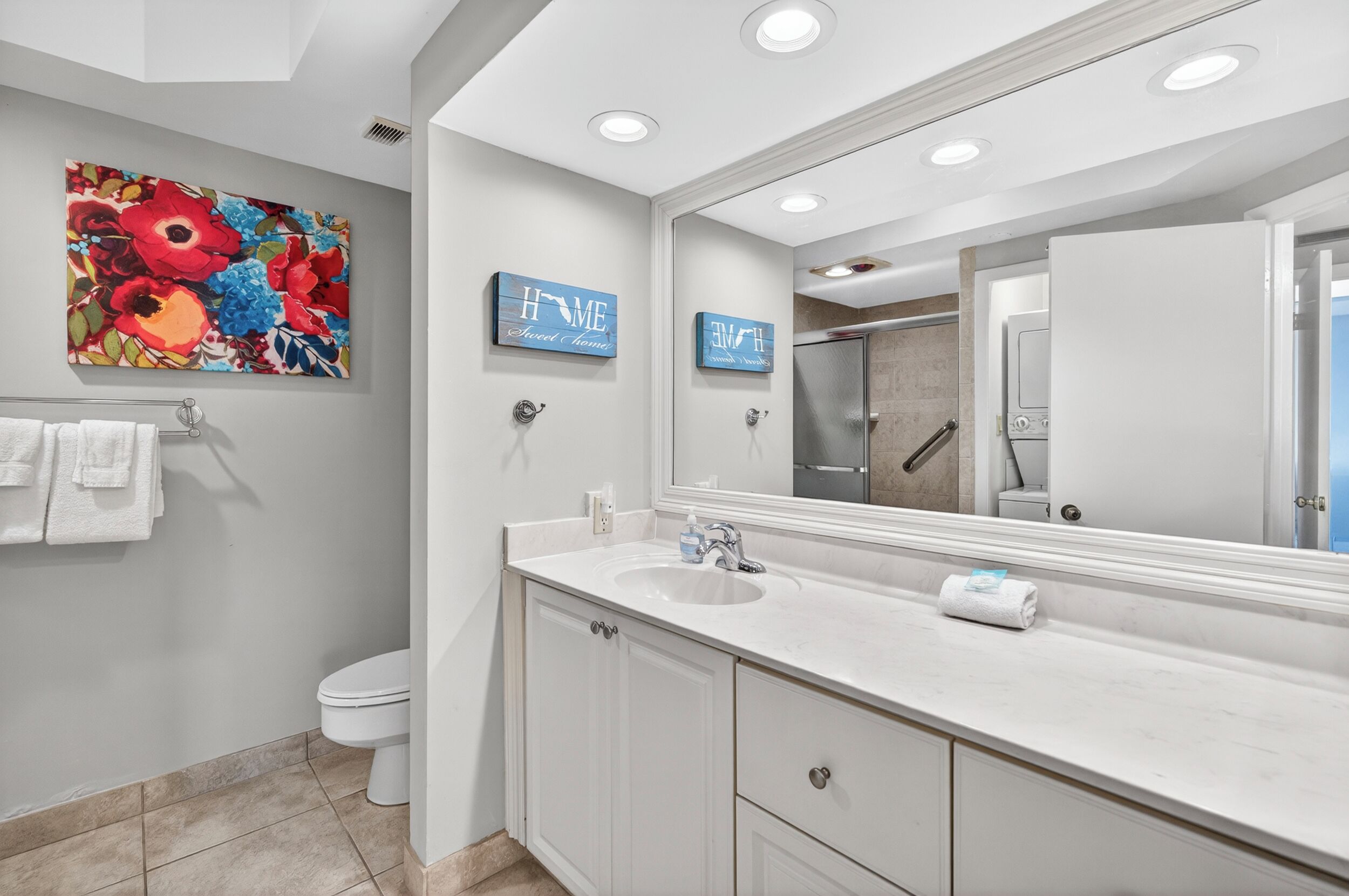 Une salle de bain moderne avec un grand miroir, des meubles blancs, un lavabo et des toilettes.