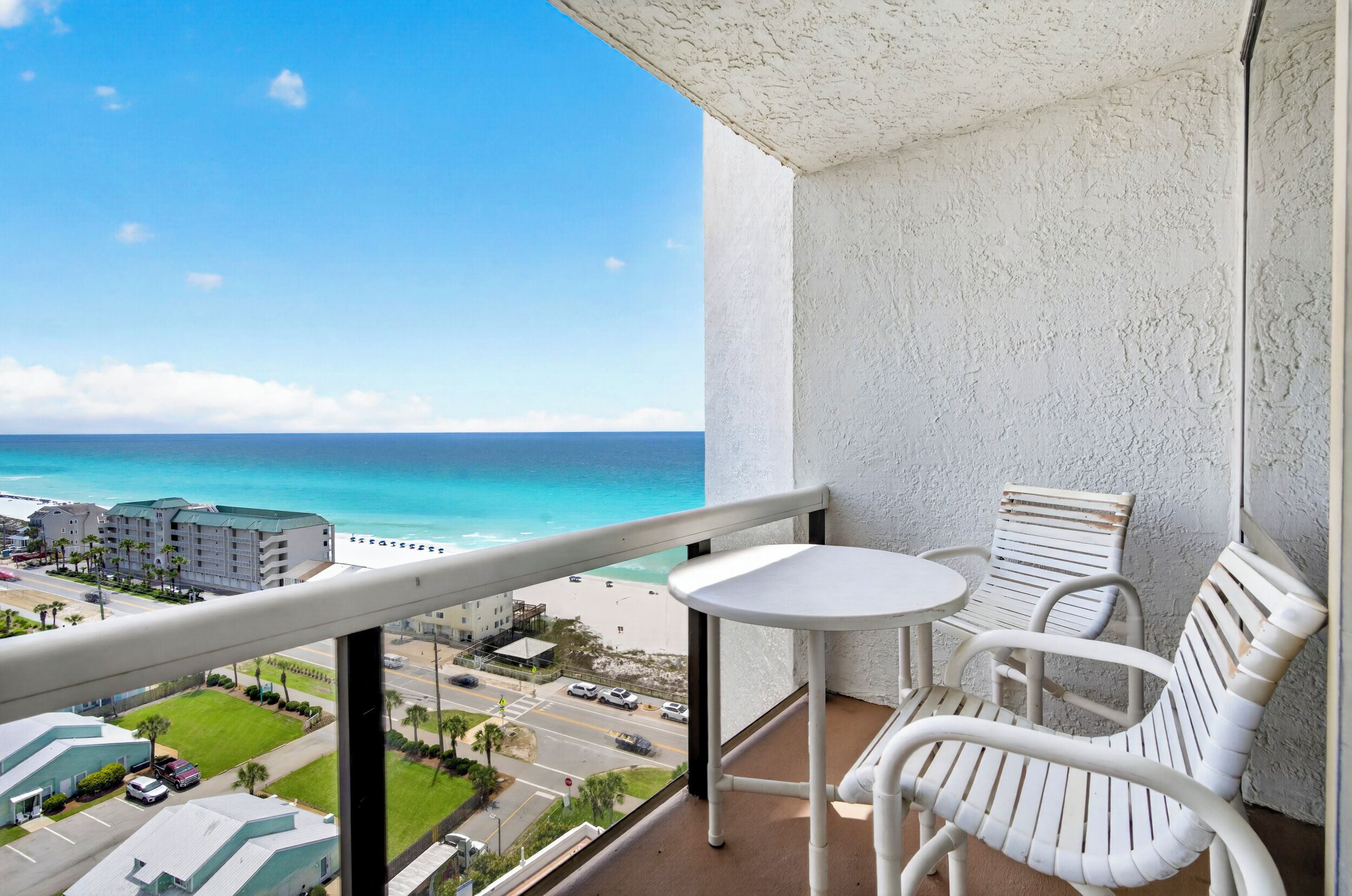 Un balcón con vista a la playa, mobiliario de mimbre blanco y una pequeña mesa.