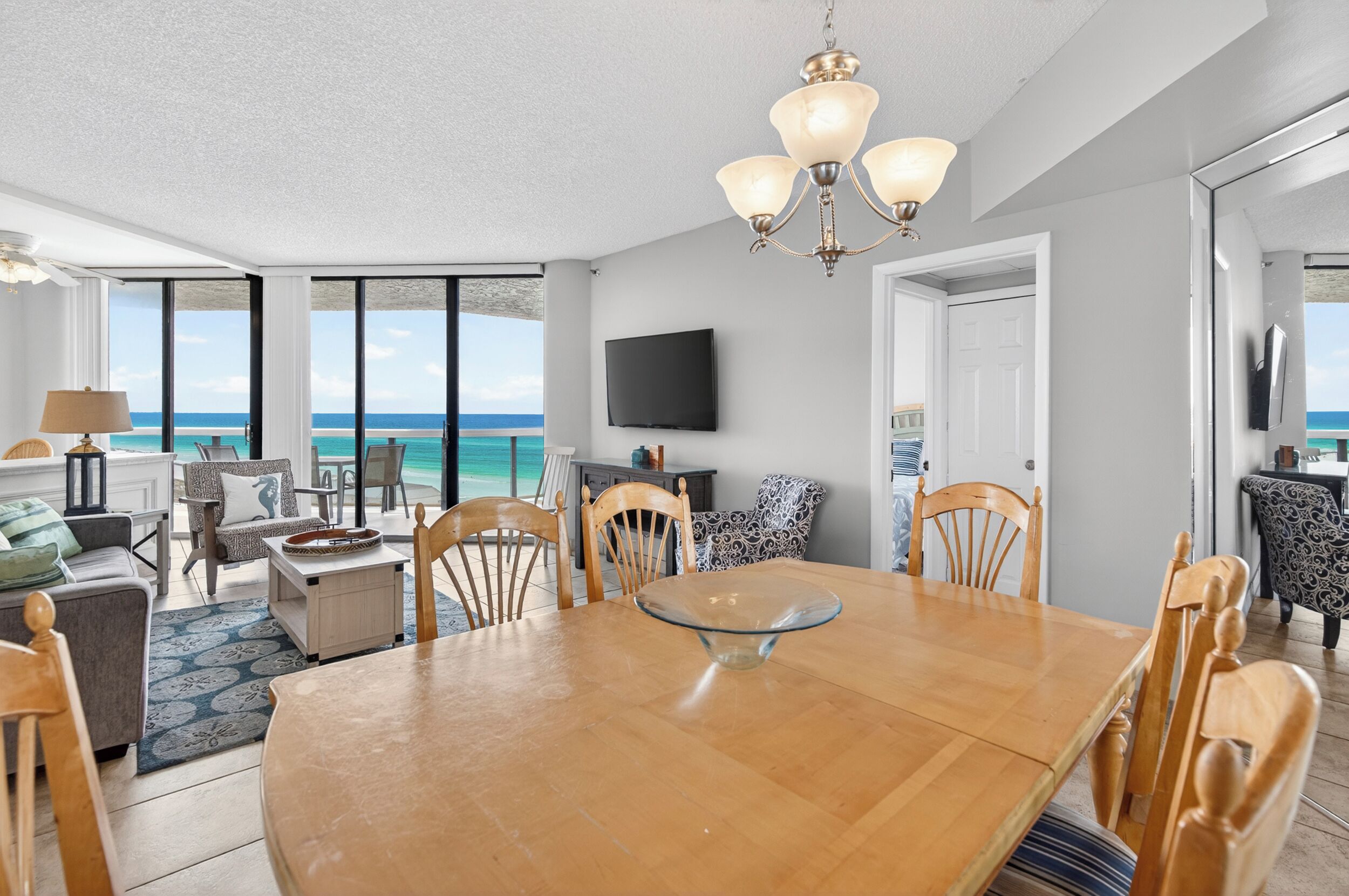 A spacious living area with a large wooden dining table, comfortable seating, a flat-screen TV, and a view of the ocean.
