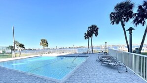 A swimming pool with a tiled deck, palm trees, and a view of the sea. - Sabine 6E- Sleeps 6 Gulf View Pensacola Beach Condo (Pensacola Beach)