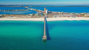 An aerial view of a coastal area with a prominent pier extending into the turquoise waters. - Sabine 6E- Sleeps 6 Gulf View Pensacola Beach Condo (Pensacola Beach)