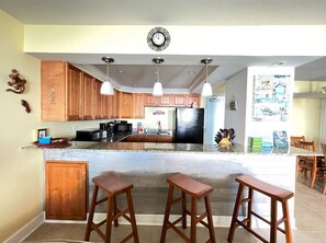 A kitchen with wooden cabinets, a black refrigerator, and three bar stools.