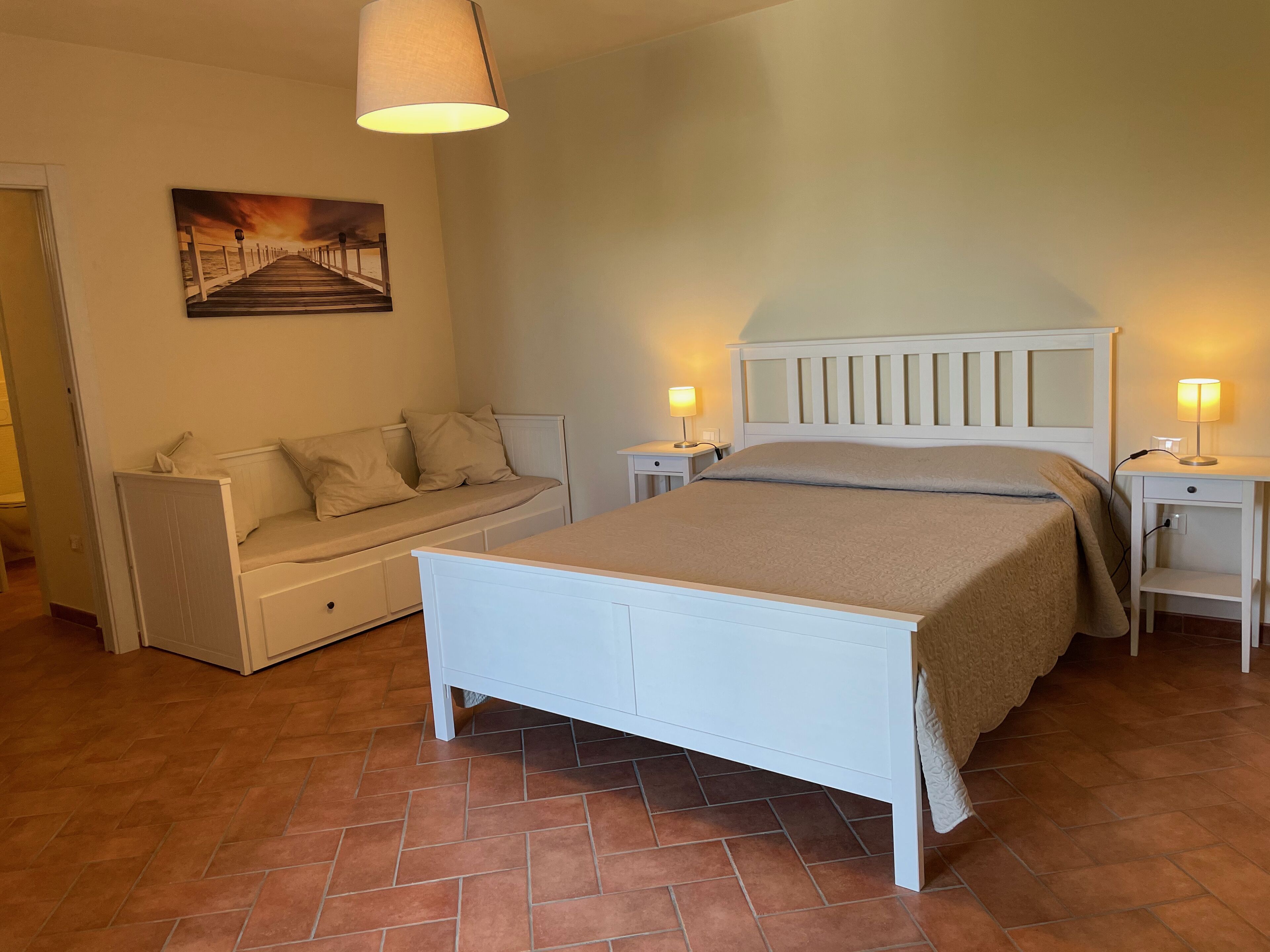 A bedroom with a bed, a sofa, a nightstand, a lamp, and a painting on the wall.