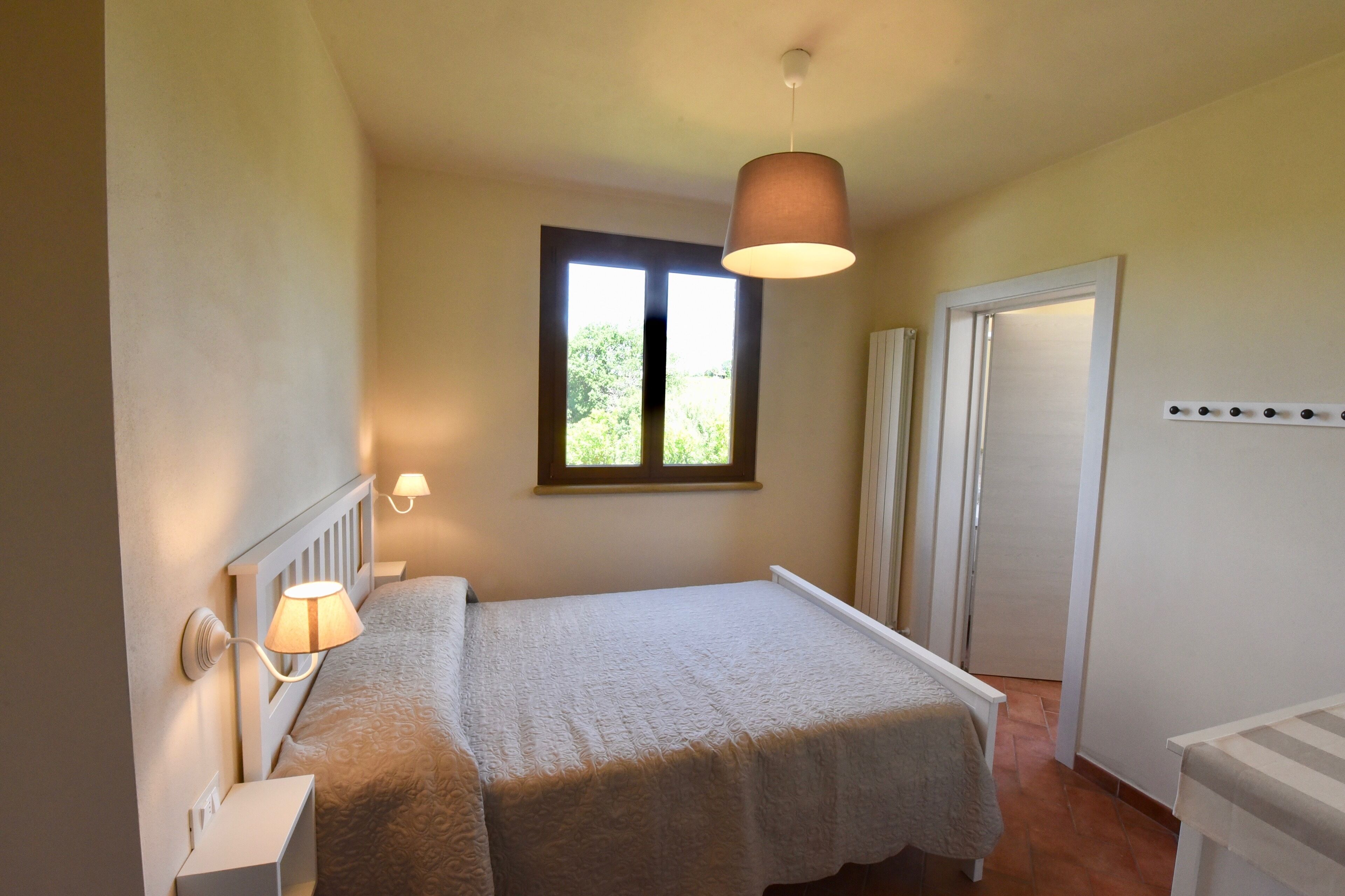 A bedroom with a bed, bedside lamps, a window, and a door.