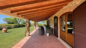 Une terrasse couverte avec un sol en briques, des piliers en pierre et des poutres en bois.