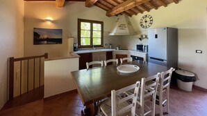 Une cuisine avec des poutres en bois, une table à manger, des chaises, une horloge, un réfrigérateur et une fenêtre.