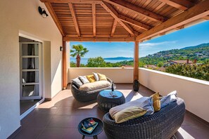 A balcony with wicker furniture, a glass table, and a view of a coastal landscape. - Villa Butterfly with Pool (Opatija)