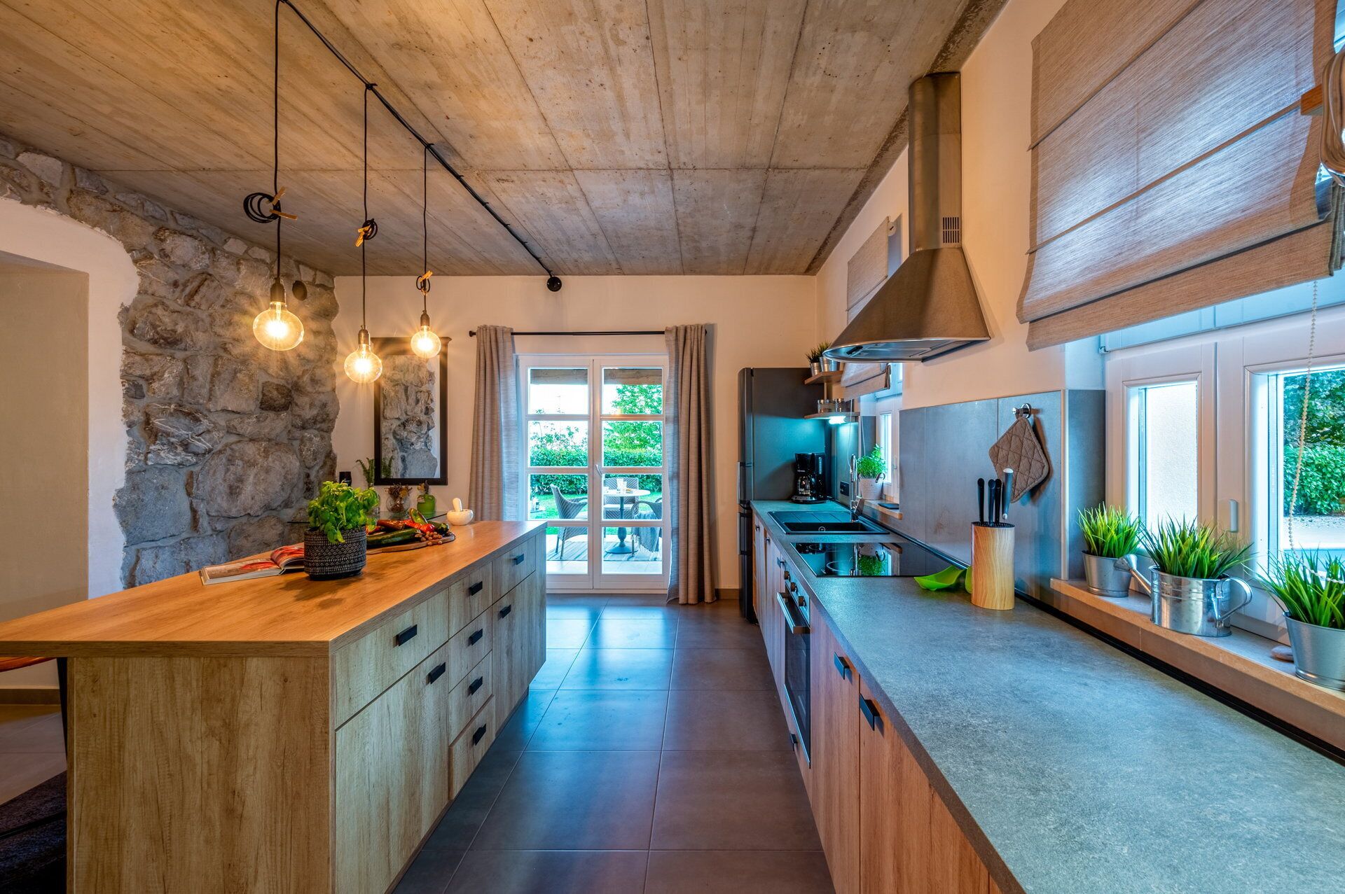 Une cuisine moderne avec un îlot central en bois, un mur en pierre et de grandes fenêtres.