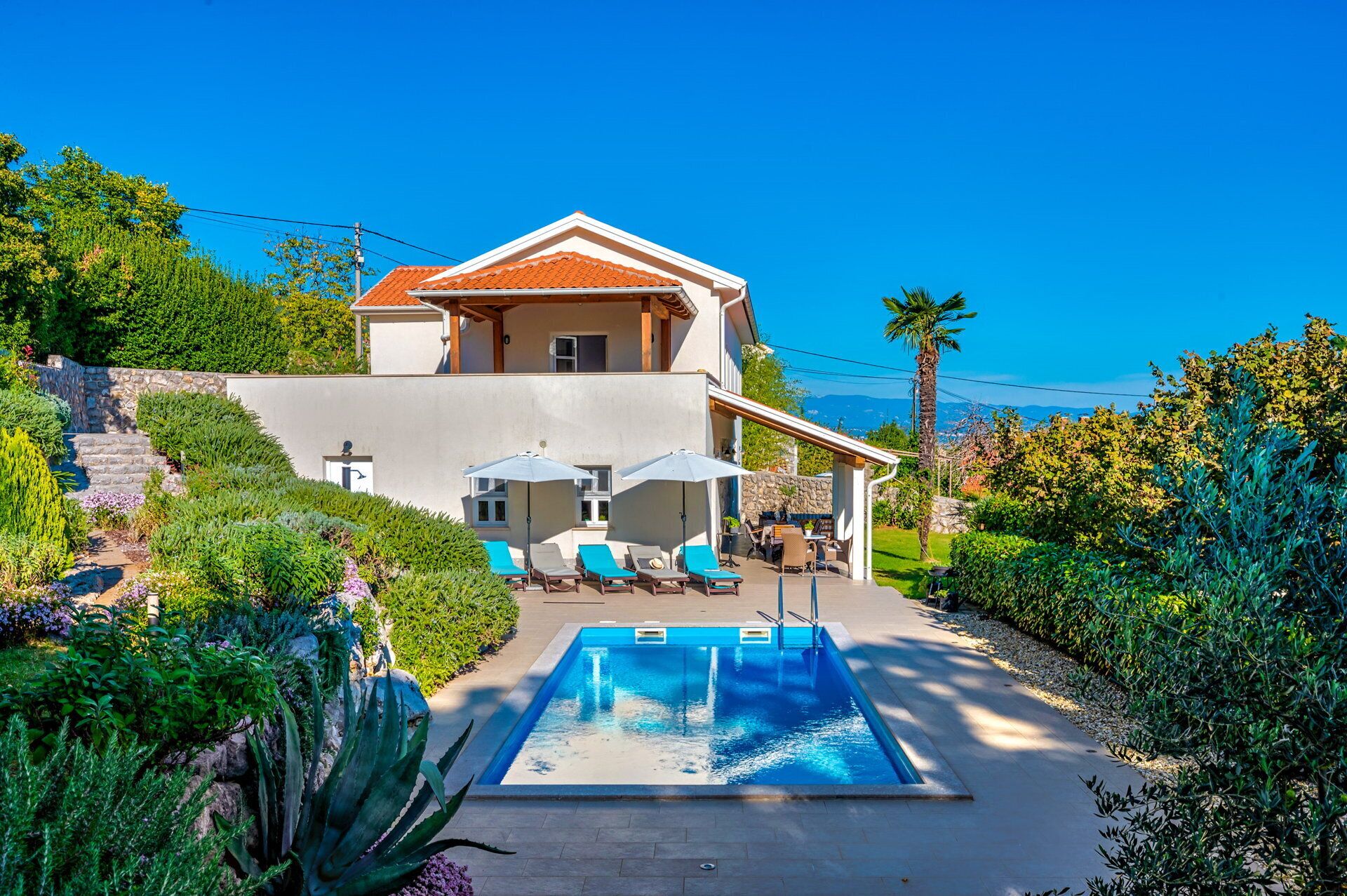 A two-story house with a swimming pool, outdoor seating, and a view of the mountains.