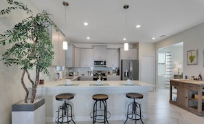 A modern kitchen with a central island, bar stools, and pendant lighting.
