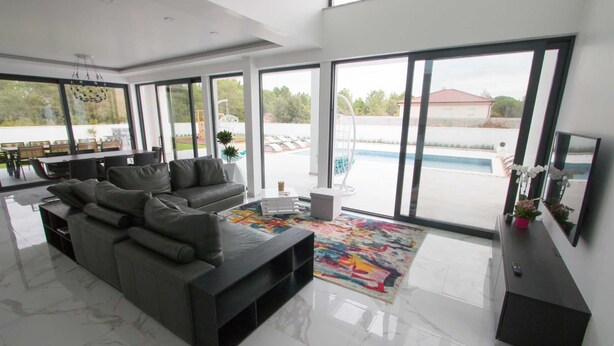 A modern living room with a large grey sofa, a coffee table, and a colorful rug. There is a TV on a black stand and a small white table with a plant. - Villa Vagabundo with Pool (Zaton)