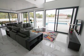 A modern living room with a large grey sofa, a coffee table, and a colorful rug. There is a TV on a black stand and a small white table with a plant. - Villa Vagabundo with Pool (Zaton)