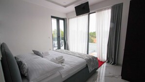 A modern hotel room with a large bed, a flat-screen TV, and a balcony with curtains. - Villa Vagabundo with Pool (Zaton)
