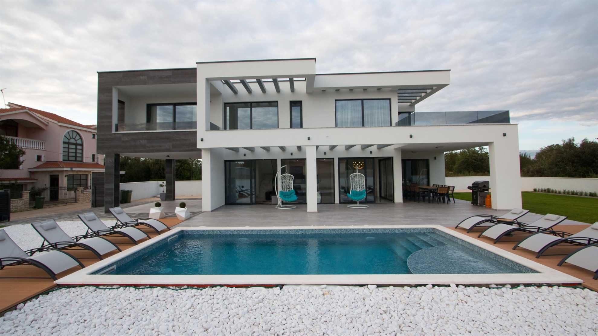 Une maison moderne à deux étages dotée d’une piscine, d’un espace salon extérieur et d’un patio.