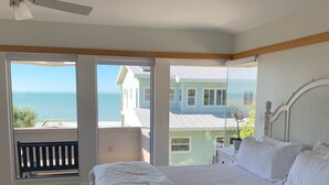 A bedroom with a large bed, a ceiling fan, and a view of the ocean through large windows.