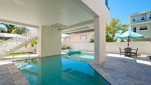 A swimming pool with a clear blue water, surrounded by a white structure, a staircase, and a table with chairs.