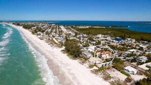 An aerial view of a coastal residential area with beachfront properties, a road, and a bridge in the distance.